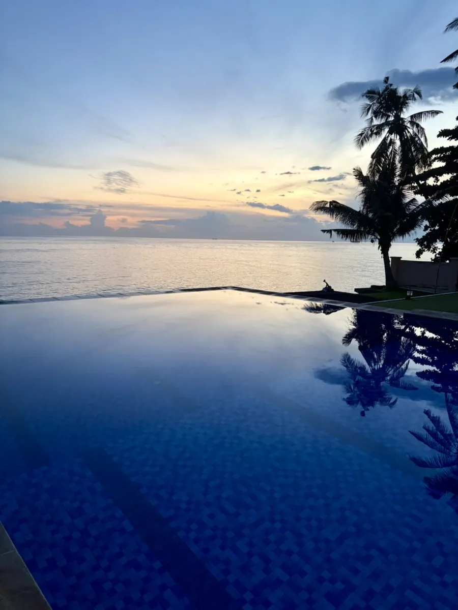 The resort's infinity pool at dusk, its edge meeting the Bali Sea